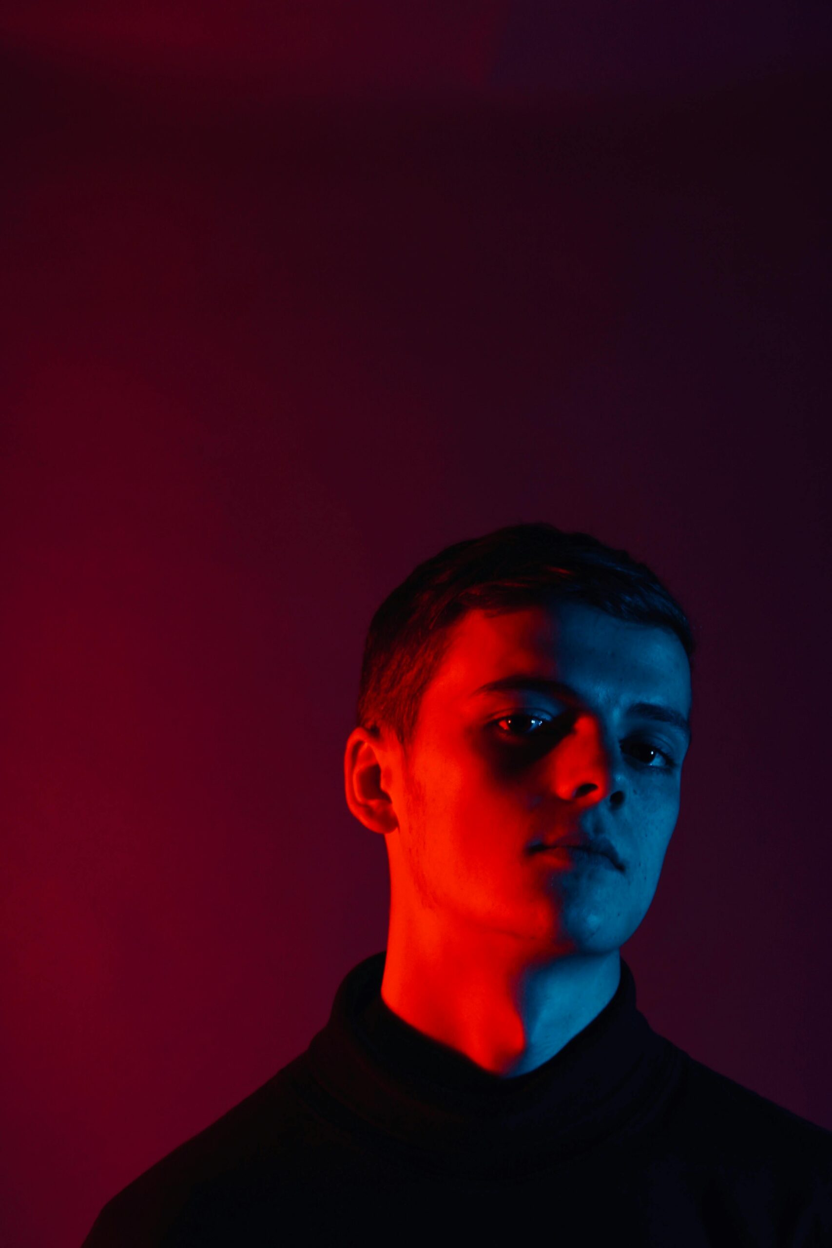 Striking studio portrait of a young man with red and blue lighting, conveying a moody atmosphere.